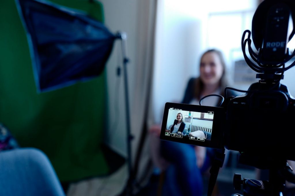 Woman being recorded in a professional studio setup, using video camera and lighting equipment.