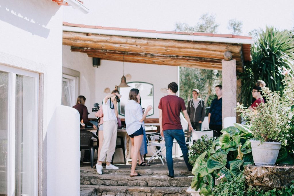 A group of young adults socializing outdoors on a sunny patio, surrounded by greenery.